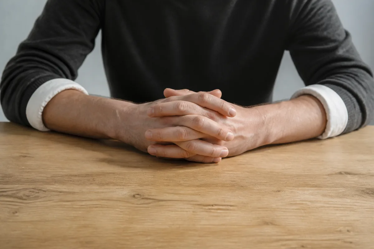 Mains croisées sur une table de bois clair entièrement nue
