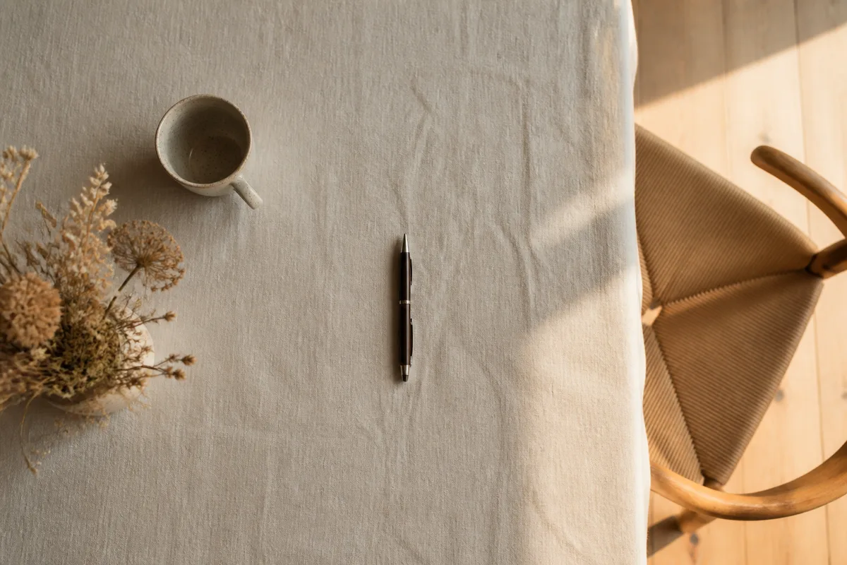 Table en lin clair avec un stylo posé, lumière de fin d&rsquo;après-midi