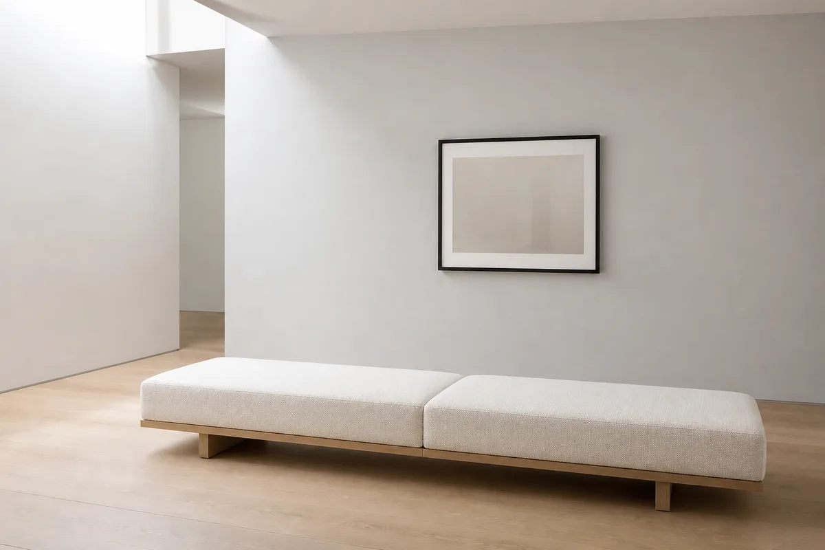 Pièce claire aux murs blancs avec un tirage encadré accroché seul, banquette en tissu écru au premier plan